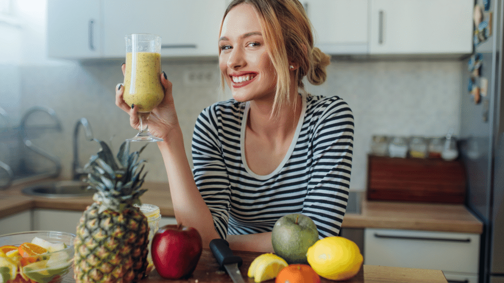 Healthy woman holding a supplement bottle in a bright kitchen with fruits and greens in the background.