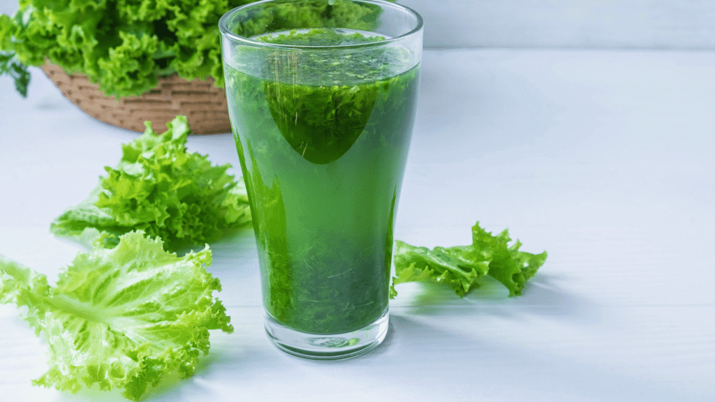 A glass of green detox juice with lemon, celery, and ginger on a white surface